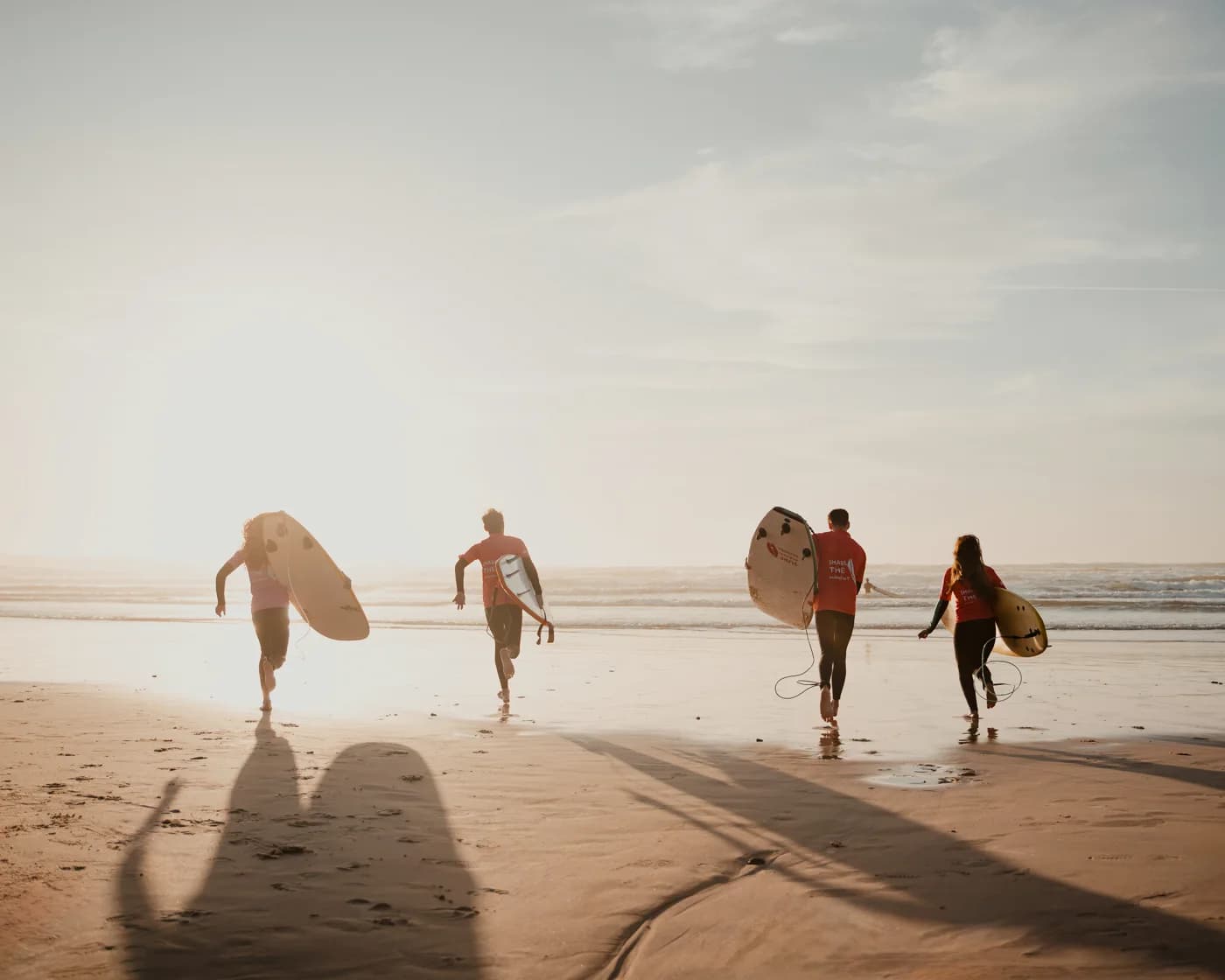A small group running to the water with boards at golden hour.