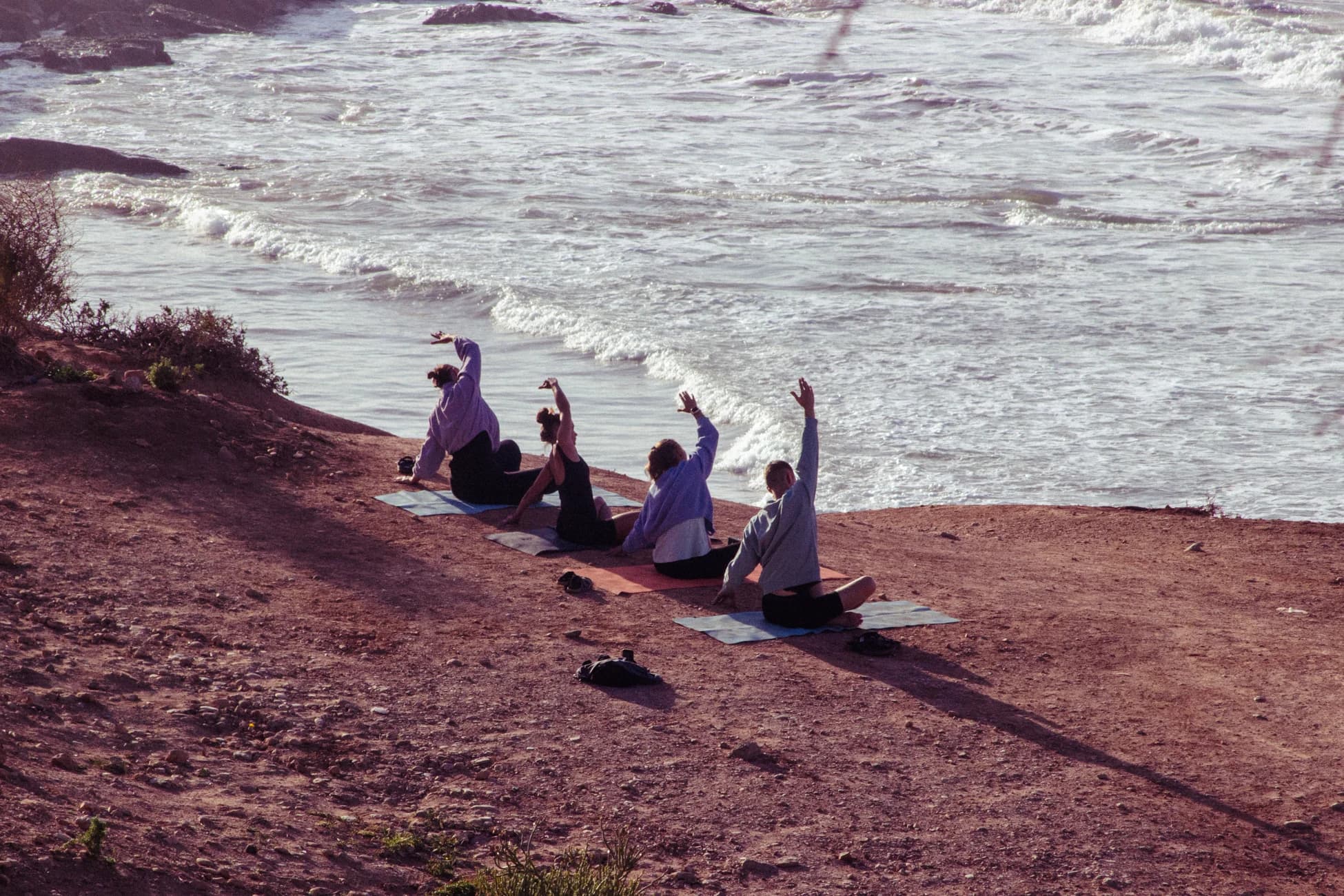 Guests in a clifftop ocean yoga session at golden hour.
