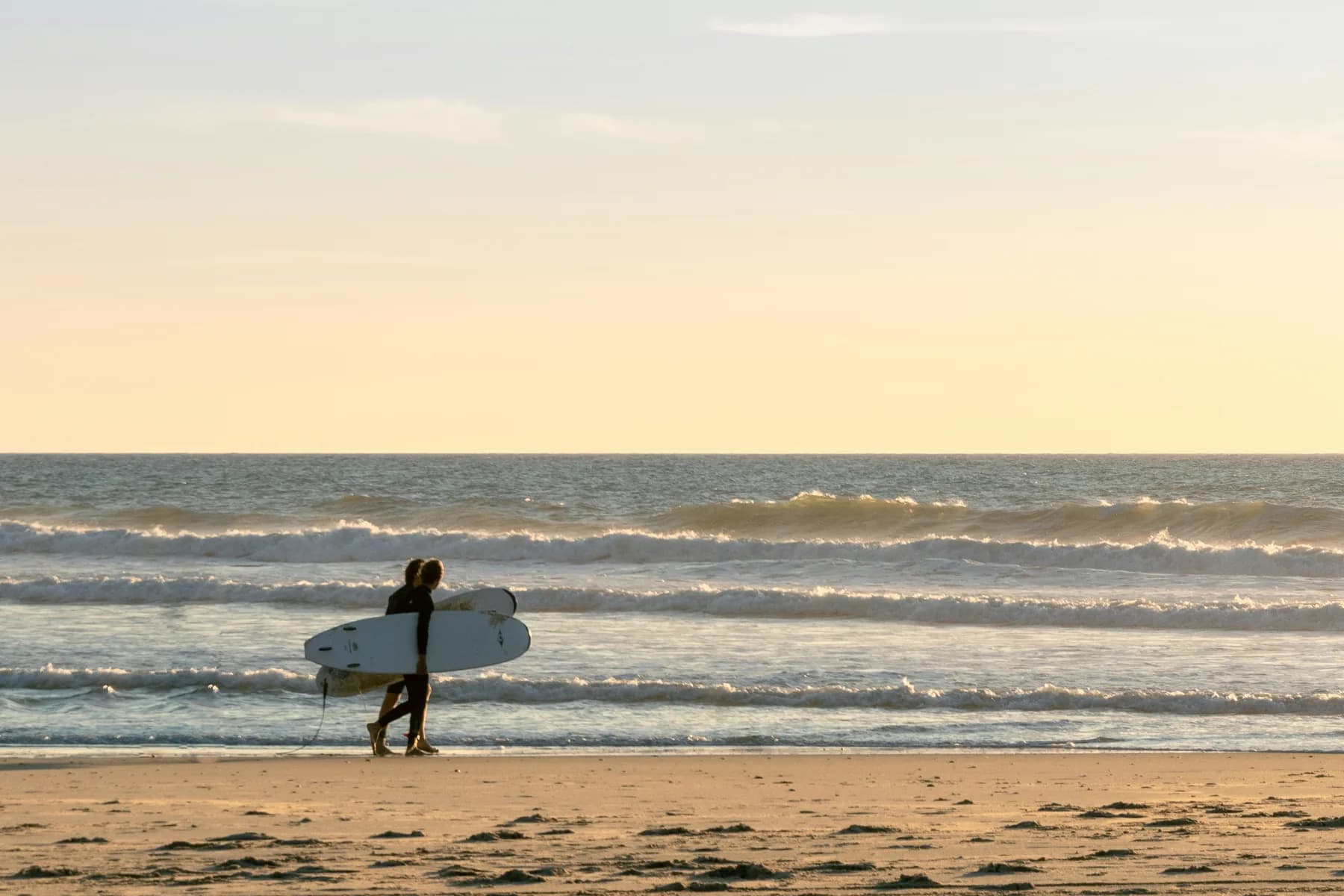A lone surfer walking the beach with a board at sunset