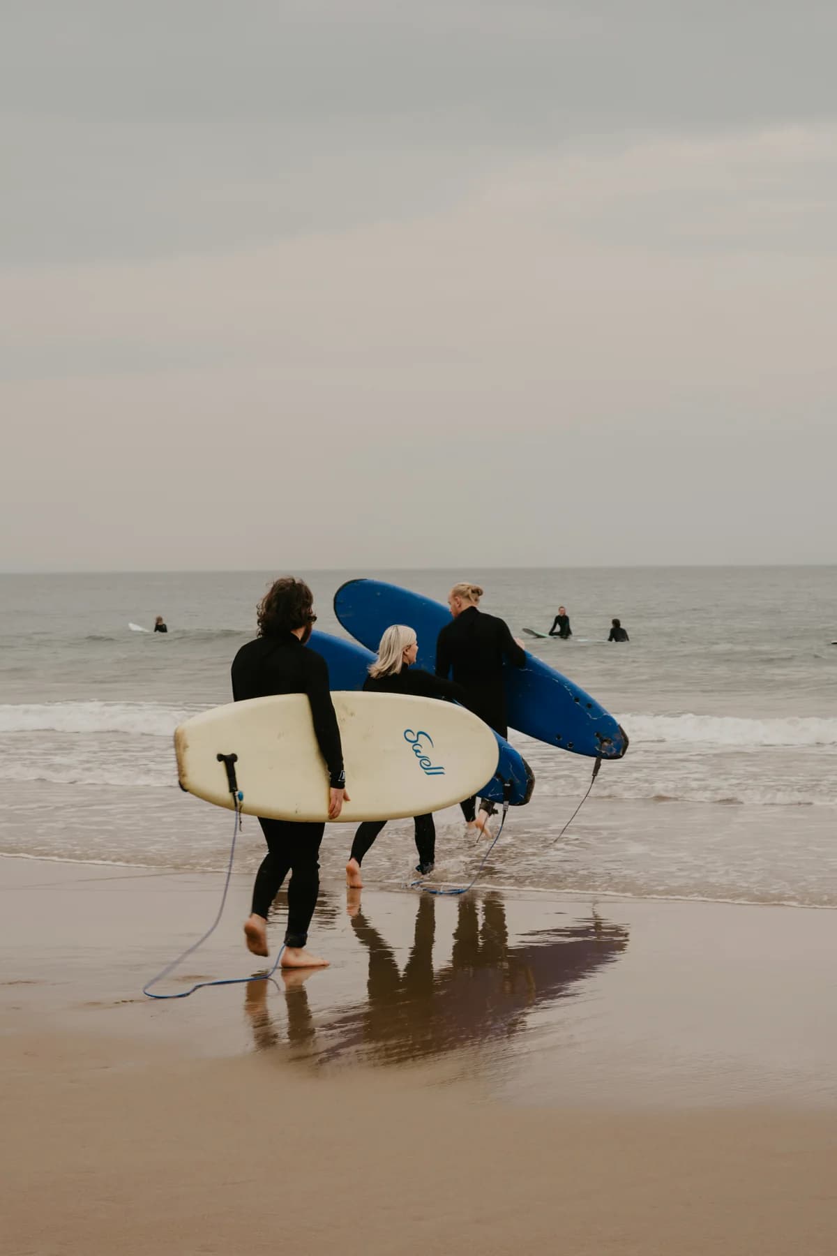 Surfers walking into the water with boards under a soft morning sky
