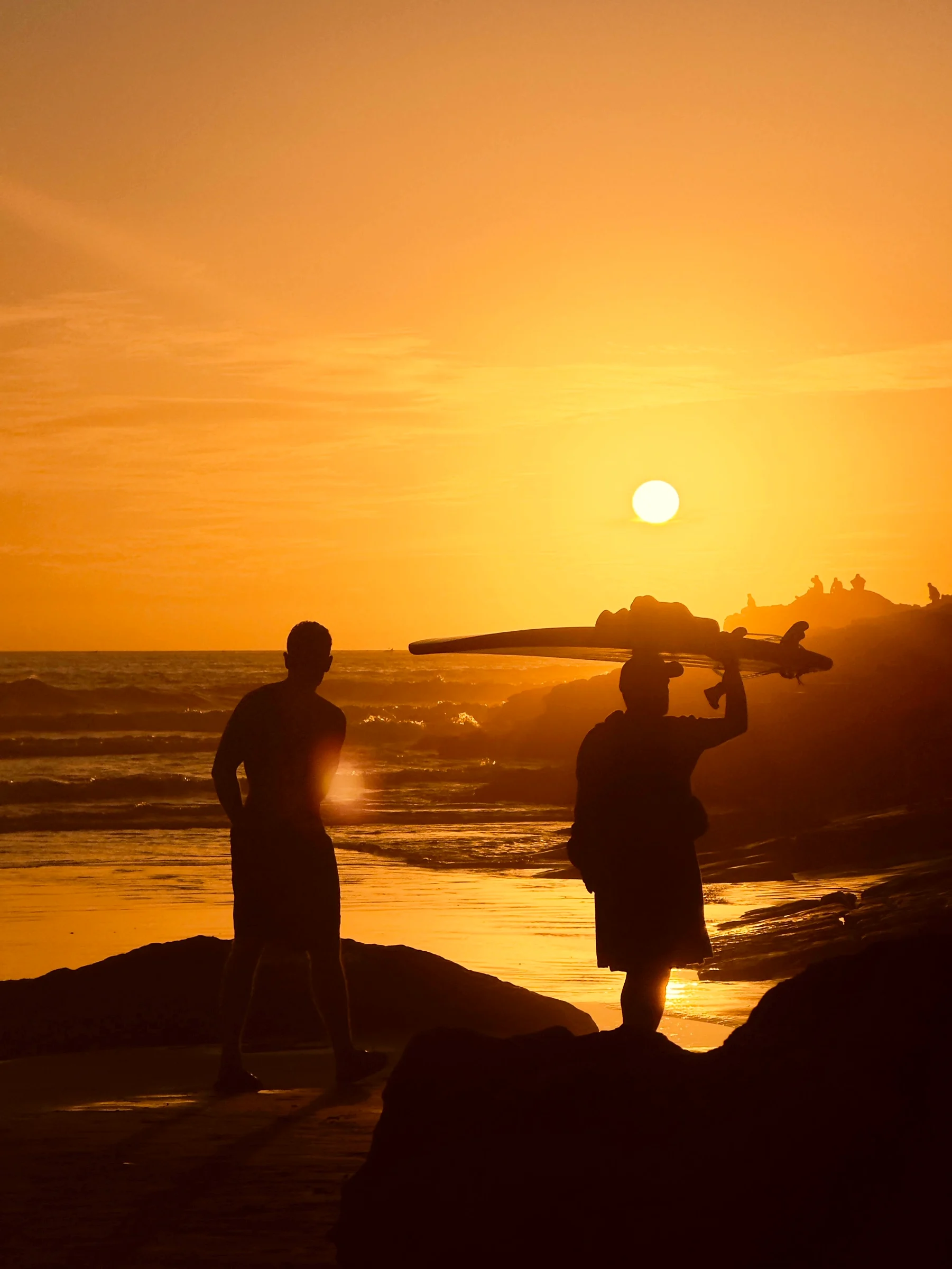 A surfer walking the shoreline at golden hour