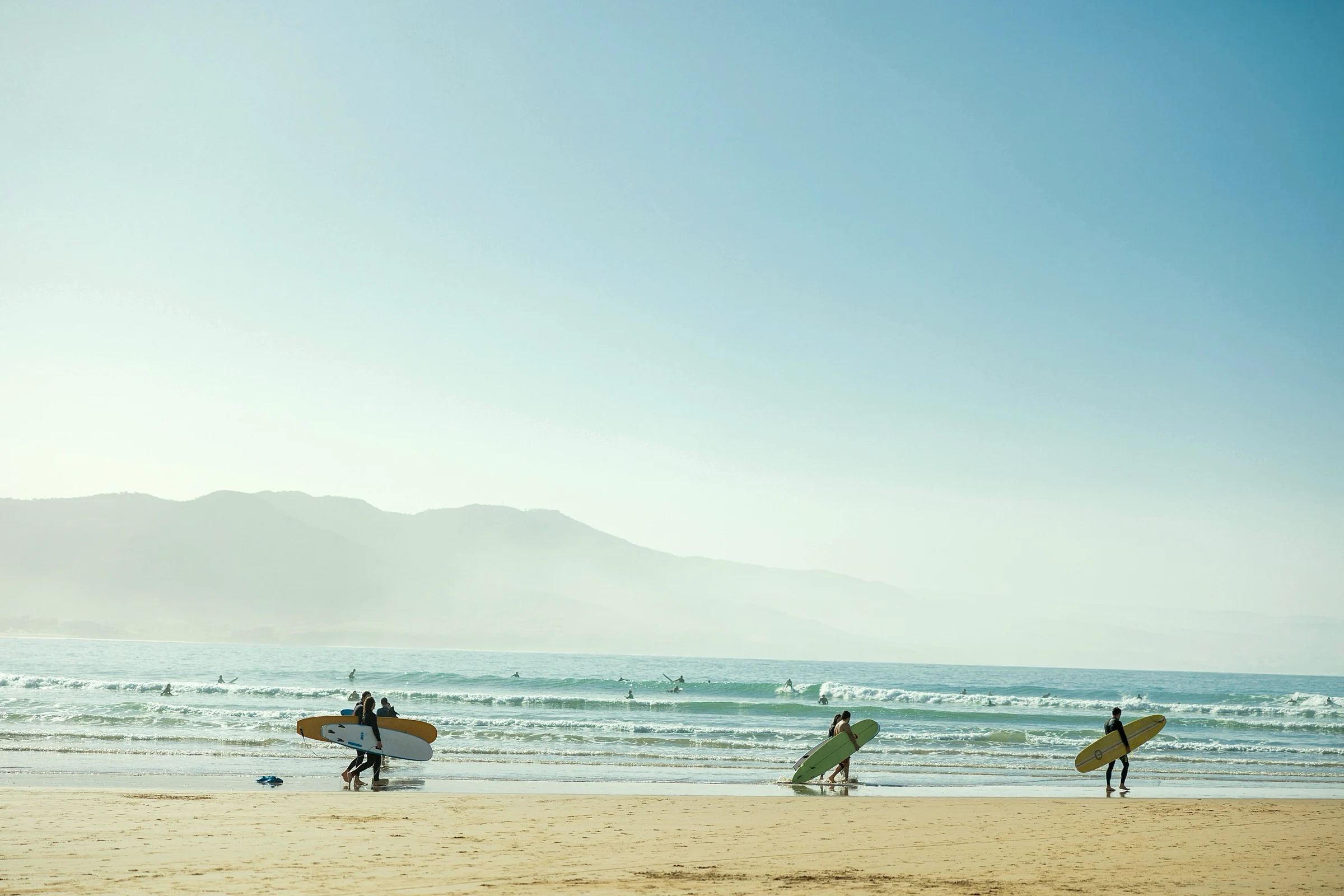 Two surfers walking Tamraght beach beneath the misty foothills